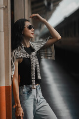 Young lady stands by a column at the train station, shading her eyes from the sunlight as she waits for the train