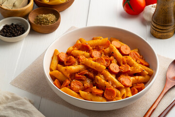 Sausage pasta,Stir fried penne rigate pasta with tomato sauce and cheddar cheese in white plate.