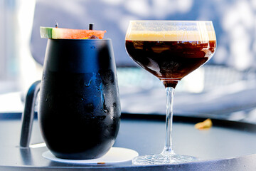 Espresso Martini Cocktail and Tequila cocktail. One cocktail is in a classic coupe glass and the other is in a modern black metal tin. The espresso martini has two layers contrasting dark and light. 
