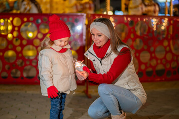 A mother and her young daughter, both wearing cheerful red hats and scarves,  in a bustling Christmas market. The twinkling lights and decorated stalls create a magical atmosphere.