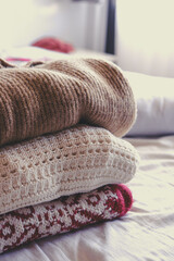 Stack of clean freshly laundered, neatly folded women's clothes on bed. Pile of shirts and sweaters on the bed. Copy space, close up