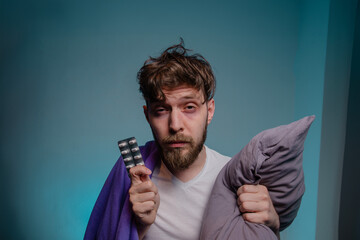 Man having insomnia problems holding blanket and medicine in hands, dark circles under eyes