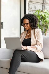 A woman is sitting on a couch and using a laptop. She is smiling and she is enjoying herself