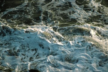 Close-up view of white foam breaking against dark ocean rocks