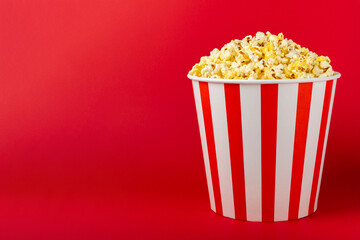 Popcorn box. Red and white striped buckets of salted popcorn on a red background. Cinema and entertainment concept. Movie night with popcorn. Delicious appetizer, snack. Place for text.