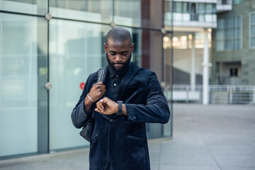 black businessman in suit with backpack checks time on wristwatch with annoyed and upset expression