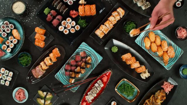 Top view of traditional japanese cuisine . Sushi rolls set with salmon , tuna fish and vegetable served on black stone table . Asian food on black stone slate with chopsticks . Camera movement .