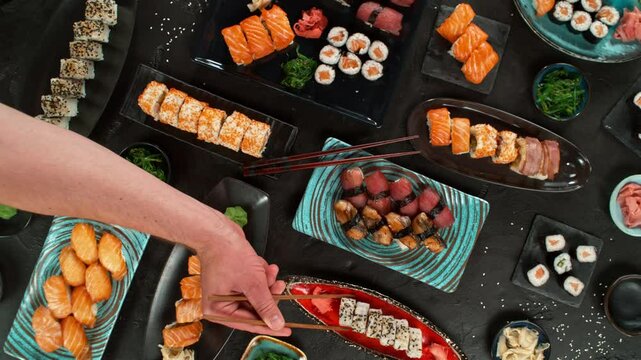 Top view of traditional japanese cuisine . Sushi rolls set with salmon , tuna fish and vegetable served on black stone table . Asian food on black stone slate with chopsticks . Camera movement .