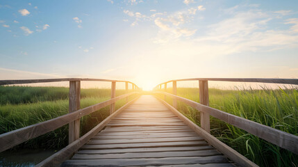 Obraz premium Scenic wooden bridge over grassy wetlands at sunrise, offering a peaceful and serene landscape view.
