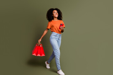 Full length photo of charming positive woman wear orange t-shirt reading modern gadget rising shoppers isolated khaki color background