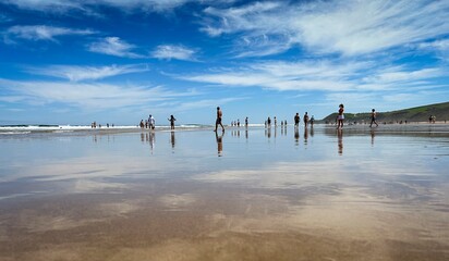 Panoramic view of the beach of Gerra, in Cantabria. with the sky and some people walking on the beach and reflected in the wet sand.