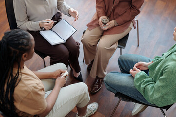 High angle of several patients and female psychologist sitting on chairs in front of each other and discussing psychological problems