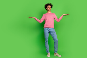 Full length photo of uncertain funny guy wear pink sweater comparing arms emtpy space isolated green color background