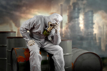 A man in a gas mask and protective suit sitting on a barrel of chemical waste. Environmental pollution concept. Dirty air with dust and noise, grunge effect.