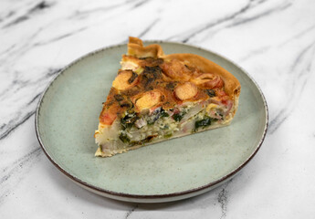 Closeup view of a slice of healthy crab sticks and vegetables tart on the white marble table	
