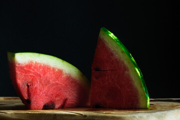 Close-up of watermelon slices on a wooden table with black background