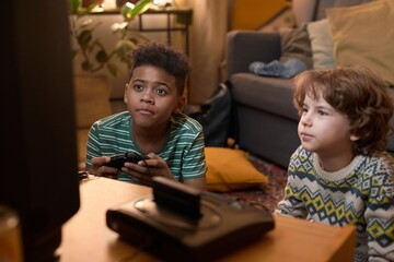 African American teen boy with short curly hair and his brown-haired Caucasian fried are deeply focused on playing retro video game