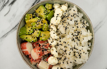Top view of an asian seafood salad made with kani kama, avocado, sushi rice, cream cheese and sesame seeds, in a bowl on the white marble table