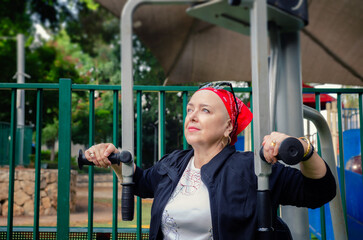 Mature woman is working out on the fitness machine. She has a bald head, indicating she is...