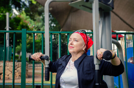 Mature woman is working out on the fitness machine. She has a bald head, indicating she is undergoing chemotherapy, a common treatment for cancer that often results in hair loss.