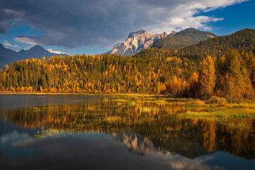 Calm lake reflecting dramatic cloudscape and autumn colors in the canadian rockies