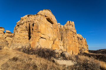 Sandstone cliff face casting shadows on grassy landscape under blue sky