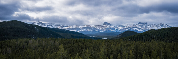 Fototapeta premium Dramatic snow covered mountain peaks towering over evergreen forest