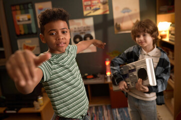 Two multiethnic teenage boys having fun listening to 80s music with a boombox in a retro-themed room decorated with vintage posters. Caucasian boy holding boombox