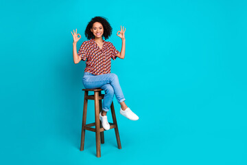 Photo of positive girl sit chair make okay symbol isolated cyan color background