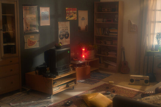 Interior of retro living room featuring a TV, boombox, guitar, bookshelf, posters, and vintage decor with warm sunlight streaming through window