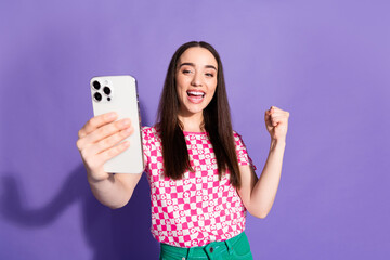 Photo portrait of attractive young woman hold device winning dressed stylish pink clothes isolated on violet color background