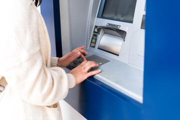 A detailed close-up shot of an unrecognizable woman’s hands typing on an ATM keypad, highlighting...
