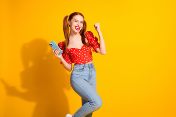 Photo portrait of lovely young lady hold device winning dressed stylish red garment isolated on yellow color background