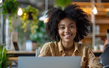 A woman with curly hair is sitting at a table with a laptop in front of her. She is smiling and she is enjoying herself