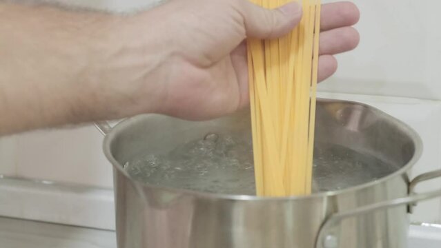 cook throws raw spaghetti into boiling water, slow motion
