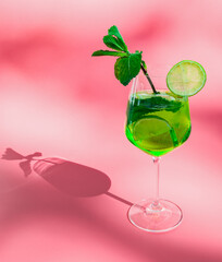 A glass of alcoholic drink mojito with green lime and mint on a pink .