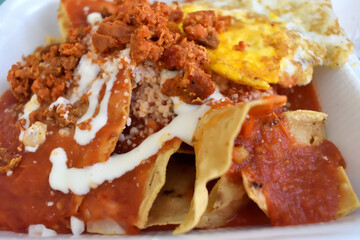 A plate of food called chilaquiles with a cream and red sauce on top and eggs, mexican