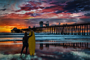 A female silhouetted surfer takes a minute to admire the colorful sunset at the Oceanside Pier, Oceanside, California, USA.