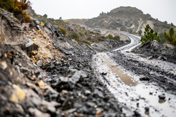 muddy wet road with rocks in mountains, dangerous landslides on mountain road
