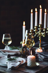 Elegant decor for Christmas family dinner. Center piece with burning candles, vintage chandelier. Zero waste eco-friendly reusable home decoration, fir tree branches. Cozy atmosphere, wooden furniture