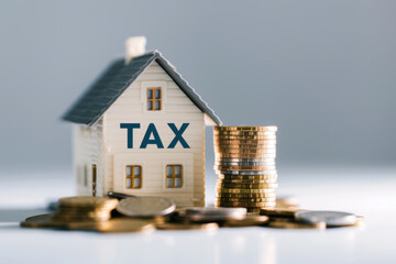 Wooden house model labeled 'tax' next to stacked coins, representing property tax and financial concepts on a blurred green background.