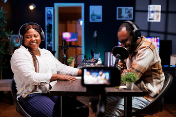 Joyful influencers in studio using professional camera to create comedy shows for live streaming channels. Cheerful social media stars working together in vlogging session using video equipment.