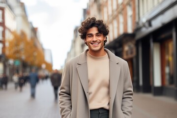 A man in a tan coat and a white shirt is smiling in front of a building