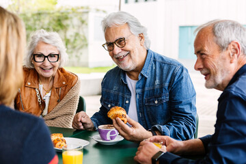 Elderly people enjoying breakfast in the morning at cafeteria bar. Retired group of mature people drinking coffee together on a weekday. Retiree people and friendship concept.