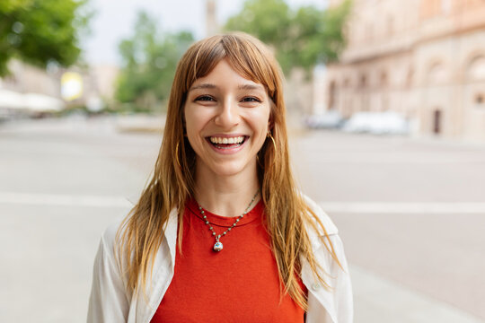 Fototapeta Happy young caucasian girl smiling at camera standing at city street. Outside portrait of joyful beautiful italian woman over urban background.