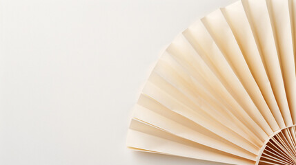 A delicate, cream-colored paper fan is partially open against a white background. Concept of beauty, tradition, and a minimal aesthetic.