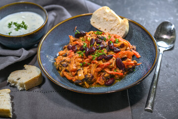 Red kidney beans, stew with bell peppers, tomatoes and onions served with a yogurt dip in blue bowls on a slate background, vegetarian levant style dish, select focus, narrow depth of field