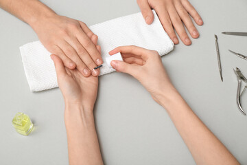 Manicure master applying cuticle oil onto male fingernails on grey background