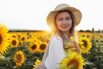 Female Farmer Holding A Bottle Of Sunflower Oil Against A Background Of Sunflowers. The Concept Of Making A Natural Product Or Harvesting. Vegan Oil. Agricultural Business. Sunlight