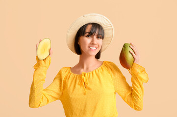 Beautiful young woman with ripe mangoes on beige background